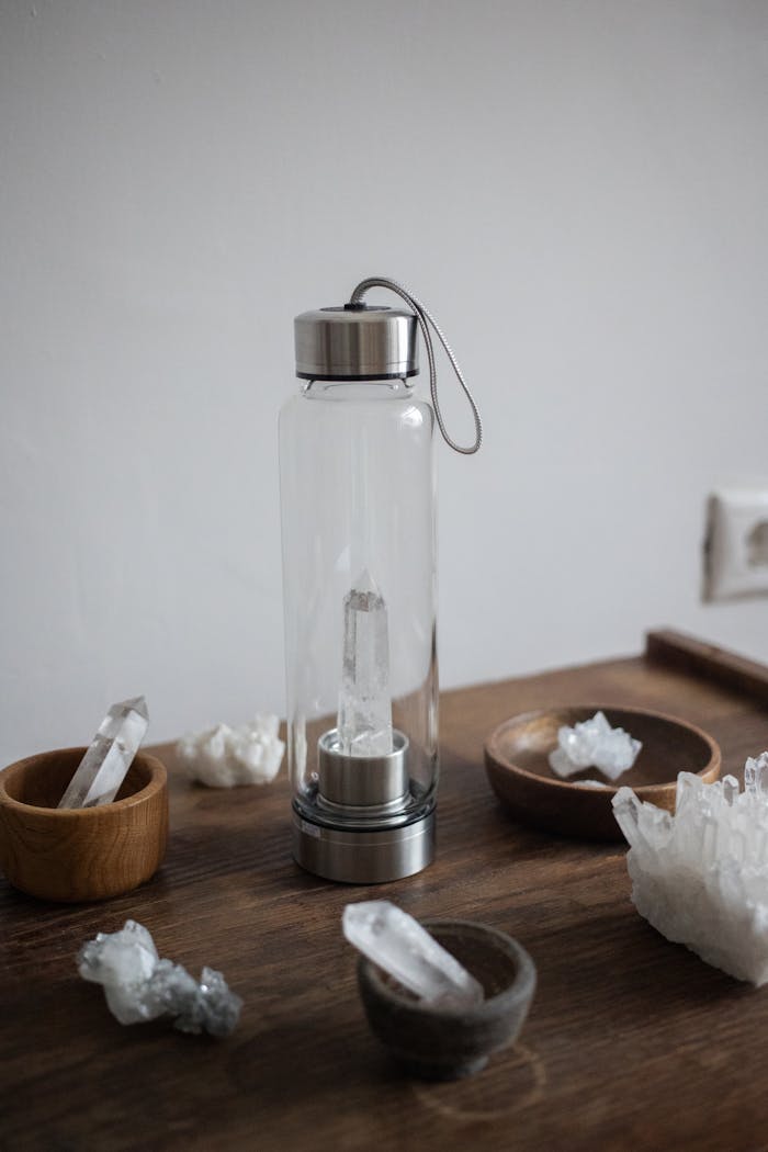 A quartz crystal infused water bottle surrounded by healing crystals on a wooden tabletop.